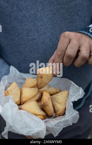 Mann hält Quark Shortbread Cookies in Dreiecke in weißem Pergamentpapier Stockfoto