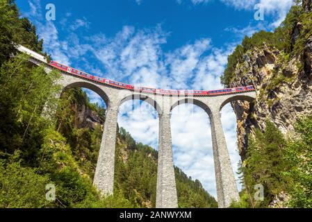 Landwasserviadukt bei Filisur, Schweiz. Es ist Wahrzeichen der Schweizer Alpen. Red Express fährt auf hohe Brücke in der alpinen Bergwelt. Malerischer Blick auf Fa Stockfoto