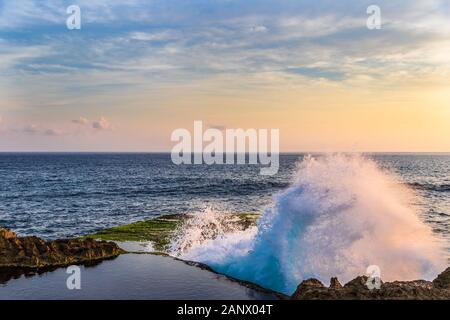 Geschwungene Welle gegen Felsen in des Teufels reißen, an der Küste von Nusa Lembongan, Bali, Indonesien. Pool von Wasser auf der Klippe im Vordergrund. Stockfoto