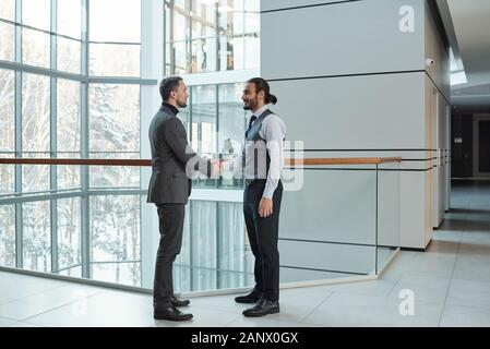 Zwei junge elegante Business Partner die Hände schütteln, während man eine andere Grußansage Stockfoto