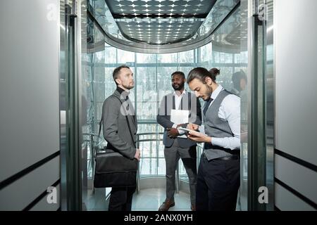 Junge gut gekleidete männliche Unternehmer mit digitalen Tablette im Aufzug Stockfoto