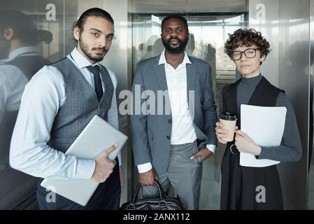 Junge Geschäftsfrau und zwei interkulturelle Geschäftsleute im Fahrstuhl bewegen Stockfoto