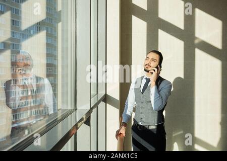 Junge elegante Geschäftsmann stehend durch die Fenster des Office Center an einem sonnigen Tag Stockfoto