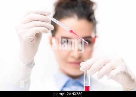 Junge weibliche Chemiker in Handschuhe fallen rote Flüssigkeit die Substanz in die neuen Impfstoff Stockfoto
