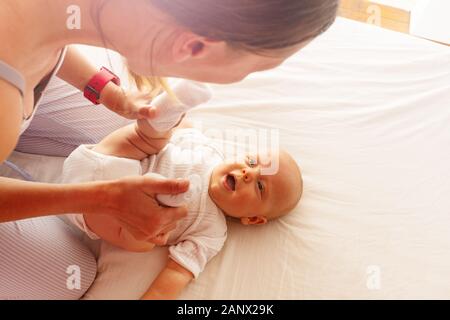 Junge glückliche Mutter halten wenig Kleinkind baby boy Holding Beine spielen im Bett Blick über Stockfoto