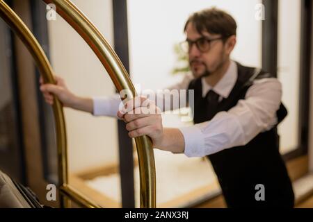 Hand von Porter Holding durch Griffe und gleichzeitig den Warenkorb und Abholung Gepäck Stockfoto