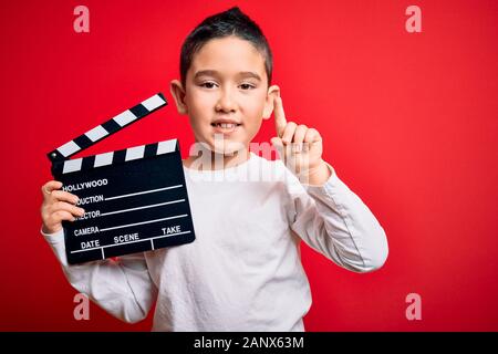 Junge junge Zicklein Dreharbeiten video Holding kino Direktor Schindeln über isolierten roten Hintergrund mit einer Idee oder Frage zeigenden Finger w überrascht Stockfoto