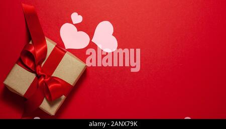 Rosa Herzen verschiedener Größe in der Nähe der braunen Papier Geschenkkarton mit einer roten Schleife. Valentines Tag Konzept. Flach Draufsicht mit Platz für Text auf r Stockfoto