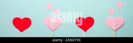 Banner Papier Herzen verschiedener Größen fliegen von rot und rosa Herzen auf Holzstäbchen auf blauem Hintergrund. Valentines Tag Konzept. Flach top vi. Stockfoto