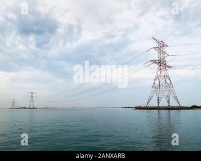 Rote und weiße overhead Strom- Leitungen und Kabel Kreuzung Wasser unterstützt durch die großen roten und weißen Pylonen in Abu Dhabi, VAE Stockfoto