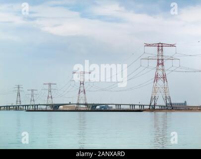 Rote und weiße overhead Strom- Leitungen und Kabel Kreuzung Wasser unterstützt durch die großen roten und weißen Pylonen in Abu Dhabi, VAE Stockfoto