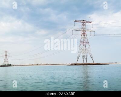 Rote und weiße overhead Strom- Leitungen und Kabel Kreuzung Wasser unterstützt durch die großen roten und weißen Pylonen in Abu Dhabi, VAE Stockfoto