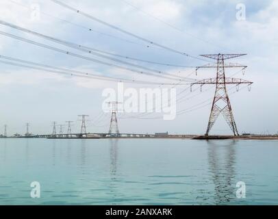 Rote und weiße overhead Strom- Leitungen und Kabel Kreuzung Wasser unterstützt durch die großen roten und weißen Pylonen in Abu Dhabi, VAE Stockfoto