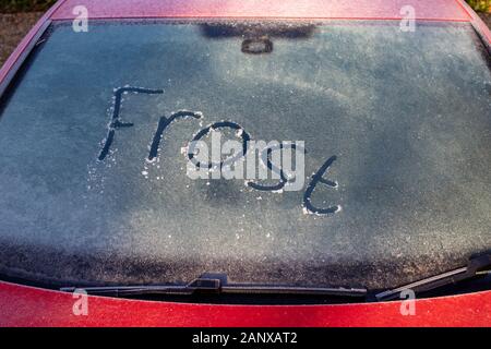 UK Wetter: das Wort Frost auf einem vereisten Windschutzscheibe von einem roten Auto auf einem kalten, frostigen Morgen im Winter, Surrey, South East England geschrieben, Großbritannien Stockfoto