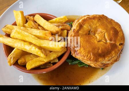 Typische deftig, lecker British Pub grub Mahlzeit: warmes Fleisch Torte in Soße mit einer Schüssel mit Golden gebratene chunky Chips auf ein weißes Porzellan Teller serviert Stockfoto