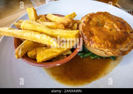 Typische deftig, lecker British Pub grub Mahlzeit: warmes Fleisch Torte in Soße mit einer Schüssel mit Golden gebratene chunky Chips auf ein weißes Porzellan Teller serviert Stockfoto