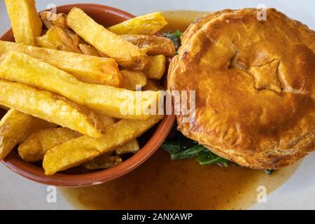 Typische deftig, lecker British Pub grub Mahlzeit: warmes Fleisch Torte in Soße mit einer Schüssel mit Golden gebratene chunky Chips auf ein weißes Porzellan Teller serviert Stockfoto