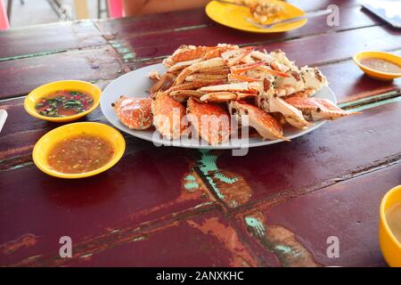 Gedünsteter Blue Crab in einer weißen Platte und einer würzigen Sauce in eine Tasse rot, Holztisch, Meeresfrüchte und lokale Küche in Thailand gekocht Stockfoto