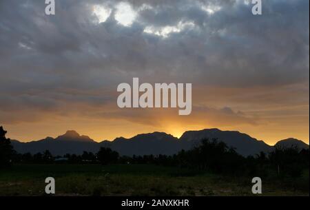 Die Silhouette der Berge und Bäume mit schwarz und orange Farbe flauschigen Wolke bei Sonnenaufgang, weiße Zuckerwatte Wolken auf die tropischen blauen Himmel bei mornin Stockfoto