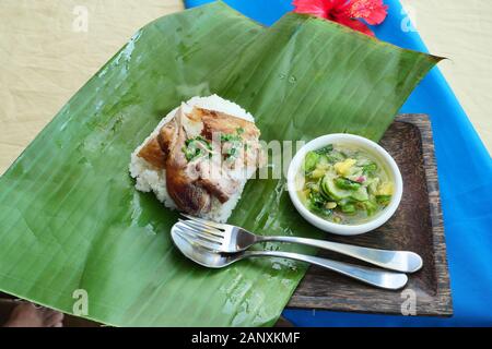 Reis garniert mit gegrilltem Hähnchen mit Löffel und Gabel auf Green Banana Leaf, Sauce aus Chili, Salz, Zitrone und Ananas in Weiß Gericht Stockfoto