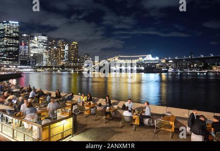 Sydney, AUSTRALIEN - 7. MÄRZ 2018 - Freunde und Touristen, die das lebhafte Nachtleben von Sydney vor einem Kreuzfahrtschiff genießen, das im Circular Quay verankert ist Stockfoto