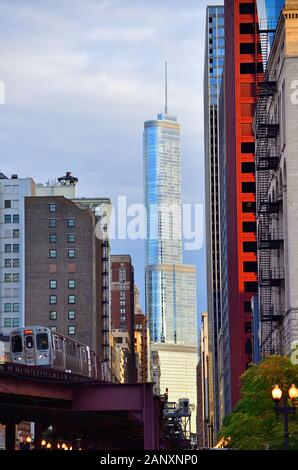 Chicago, Illinois, USA. Das Trump International Hotel and Tower reflektiert das Licht der aufgehenden Sonne, während ein L-Zug in den Canyon der Wabash Avenue einsteigt. Stockfoto