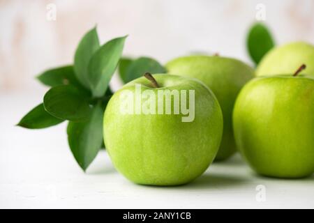 Grüne Äpfel mit grünen Blättern auf weißen Tisch Detailansicht. Gesunde knackig frische Früchte