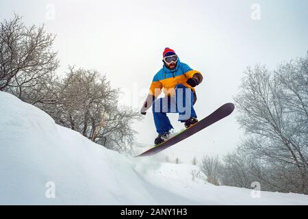 Der Kerl ist das Snowboarden. Springt er aus einem verschneiten Hügel. Snowboarden in den frischen Schnee. Winter Spaß Stockfoto