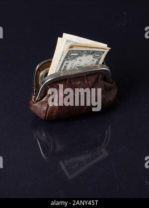 Eine offene braune Geldbörse mit Dollarnoten im Inneren auf dunklem Hintergrund Oberfläche reflektiert. Stockfoto