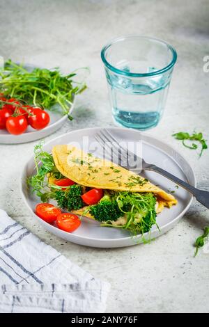 Vegan kichererbse Omelette mit Brokkoli, Tomaten und Pflanzgut auf eine graue Platte. Gesunde vegane Ernährung Konzept. Stockfoto