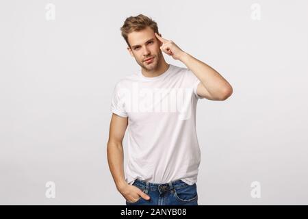 Schön freche junge blonde Kerl mit im weißen T-Shirt, Tilt Head Borsten und lächelnd Selbstbewusst, selbstsicher, selbstbewussten Blick der Kamera machen, berühren. Stockfoto