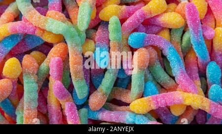 Haufen von neonzuckerhaltigen Gummiwürmern oder keuligen sauren Raupen Hintergrund. Nahaufnahme von bunten und aromatischen süßen und sauren Leckereien, die in Zuckerkristallen beschichtet sind Stockfoto