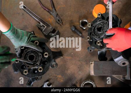 Overhead-Ansicht von Maschinenbauingenieuren, die als Team zusammenarbeiten und Autoteile auf einer Werkbank mit Metallhandwerkzeugen reparieren und überholen und dabei eine schützende Arbeitskleidung tragen Stockfoto