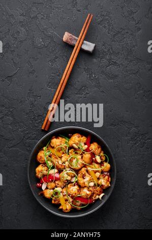 Kung Pao Blumenkohl an dunklen Schiefer Hintergrund. Sichuan Kung Pao Blumenkohl ist chinesische Küche vegetarisches Gericht mit Chili peppers, Erdnüsse, Saucen ein Stockfoto