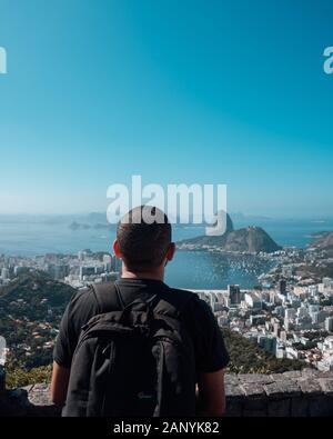 Rio DE JANEIRO, BRASILIEN - 10. Januar 2020: Ein Männchen mit Rucksack, der die schöne Aussicht auf Brasilien mit Architektur und Meer im Hintergrund genießt Stockfoto