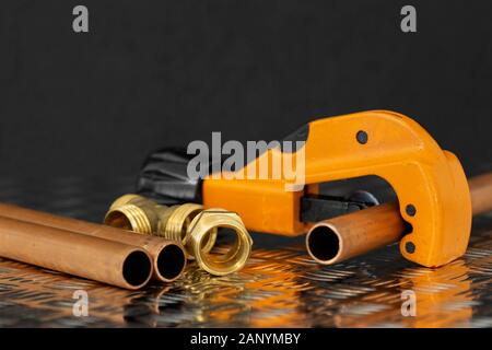 Kupferrohr und Cutter mit Leitungen Stecker auf Stahl Riffelblech Oberfläche. Sanitär Werkzeug und Ersatzteile Stockfoto