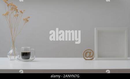 7/8 Schuß von minimalen Arbeitsbereich mit Mock up Frames, Kaffeetasse und Dekorationen auf weiße Holztisch mit weißen Wand Hintergrund Stockfoto