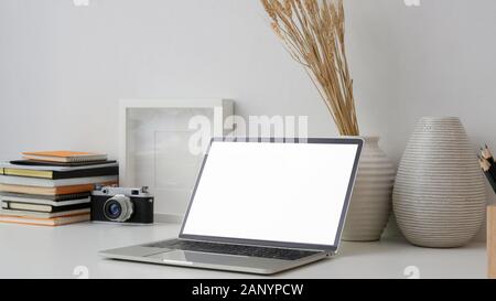 7/8 Schuß von Fotograf Arbeitsplatz mit leerer Bildschirm Laptop, Kamera, Rahmen, Büchern und Dekorationen auf weißem Schreibtisch mit weißen Wand Hintergrund Stockfoto