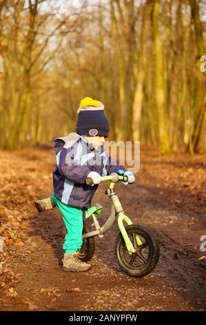 Poznan, POLEN - 12. Januar 2020: Junges zweijähriges Kind versucht, an einem kalten Wintertag auf einem kleinen Laufrad in einem Wald zu sitzen. Stockfoto
