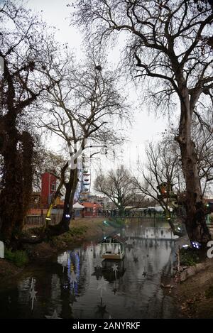 Spiegelung der Bäume in einem kleinen Teich, der Weihnachten mit dem Riesenrad im Hintergrund dekoriert ist. "Krank vor dem Elfen" Basar, Trikala, Griechenland. Stockfoto