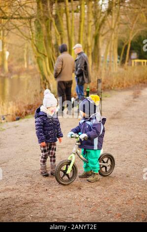 Posen, POLEN - 12. Januar 2020: Kleiner Junge auf einem Fahrrad und stehendes Mädchen im Wald von Debiec an einem kalten Wintertag. Stockfoto