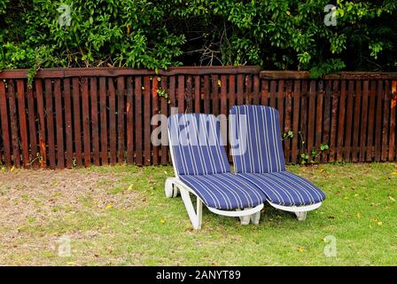 Grasfeld mit zwei Liegestühlen in der Nähe eines Holzzauns Stockfoto