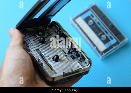 High-Angle-Aufnahme einer Person, die einen Kassettenspieler hält Mit einer Kassette auf einer blauen Oberfläche Stockfoto