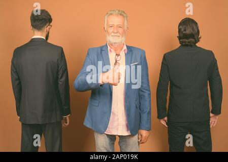 Drei multi-ethnische bärtigen Geschäftsmänner gemeinsam gegen braunen Hintergrund Stockfoto