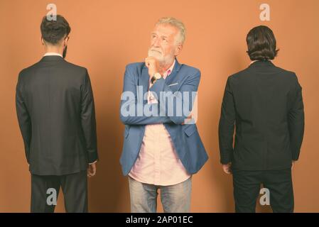 Drei multi-ethnische bärtigen Geschäftsmänner gemeinsam gegen braunen Hintergrund Stockfoto