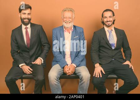 Drei multi-ethnische bärtigen Geschäftsmänner gemeinsam gegen braunen Hintergrund Stockfoto