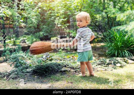 Cute adorable kaukasischen Kleinkind Junge spielt Holding Besen im Hinterhof in Garten im Freien. Kind little Helper in t-short Kurze Hose und Spaß haben Stockfoto