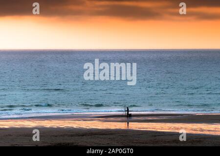 Ein einsamer Angler Angeln vom Ufer während eines intensiven Sonnenuntergang auf den Fistral in Newquay in Cornwall. Stockfoto