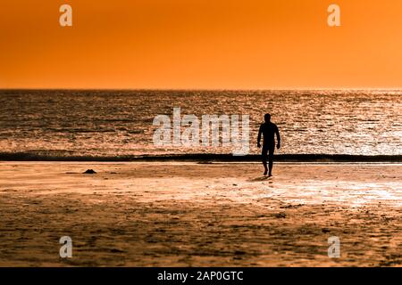 Ein Mann gehen hinunter zum Meer, wie die Sonne auf den Fistral Beach in Newquay in Cornwall. Stockfoto