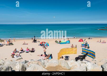 Urlauber entspannen und genießen Sie die Sonne, während Sie am Strand von Fistral in Newquay in Cornwall sonnen. Stockfoto